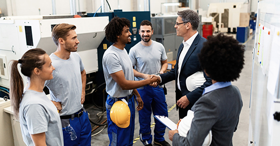 Executive shakes hands with workers on factory floor