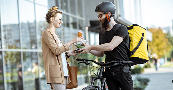 Bike messenger delivers a salad and beverage to a woman outside a building.